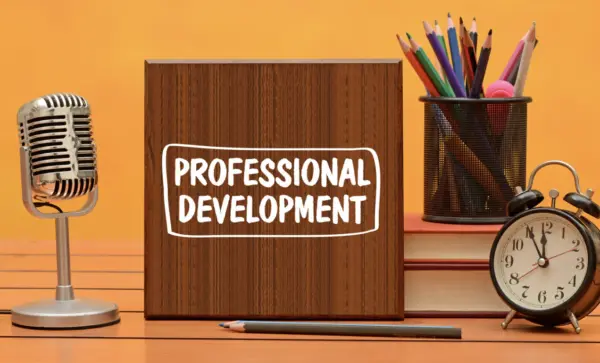 Desk with colored pencils, microphone, alarm clock, and sign reading professional development.